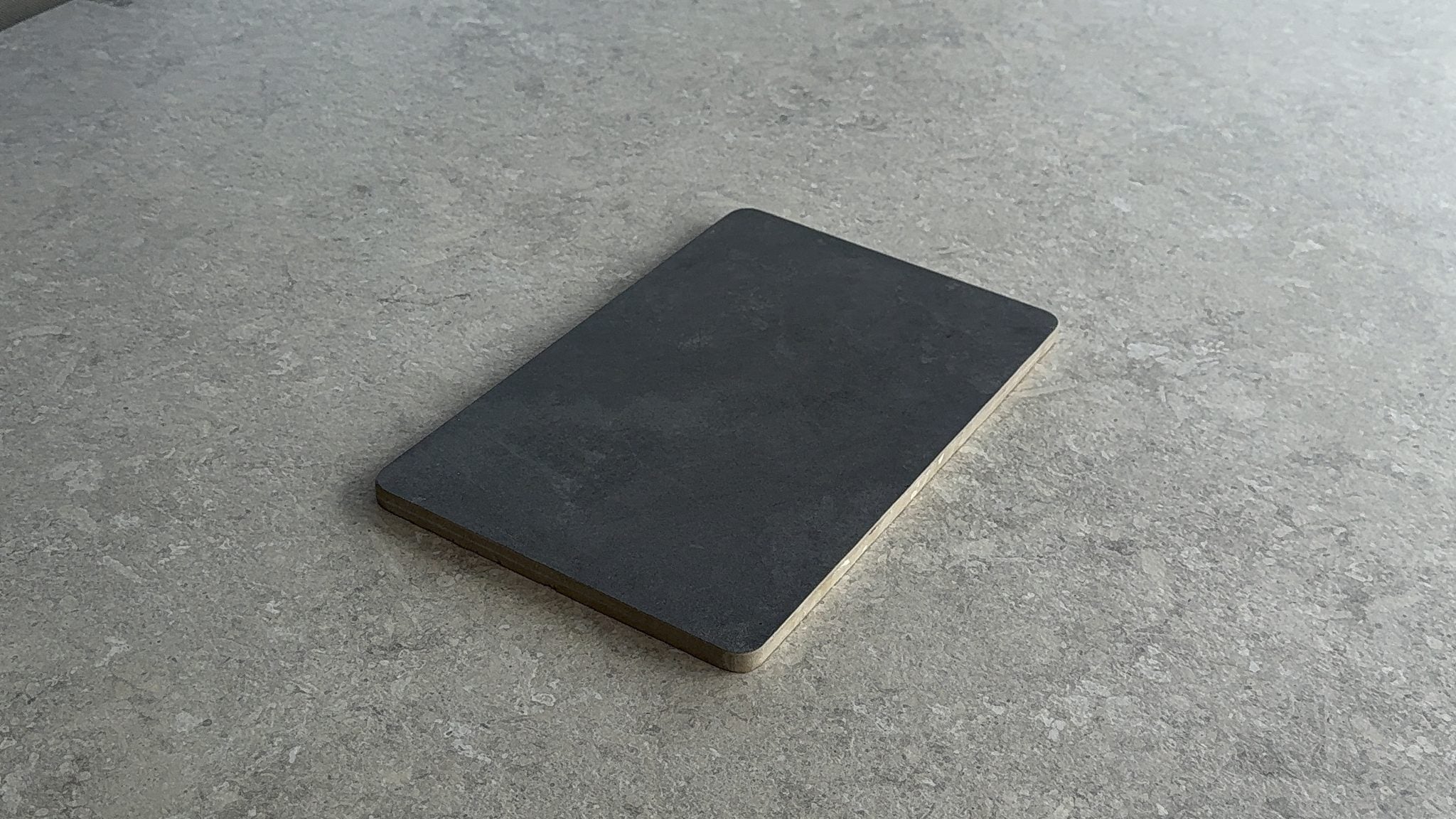 Tabla de picar FORNAX de porcelanato oscuro apoyada sobre una encimera de piedra real, sin retoques